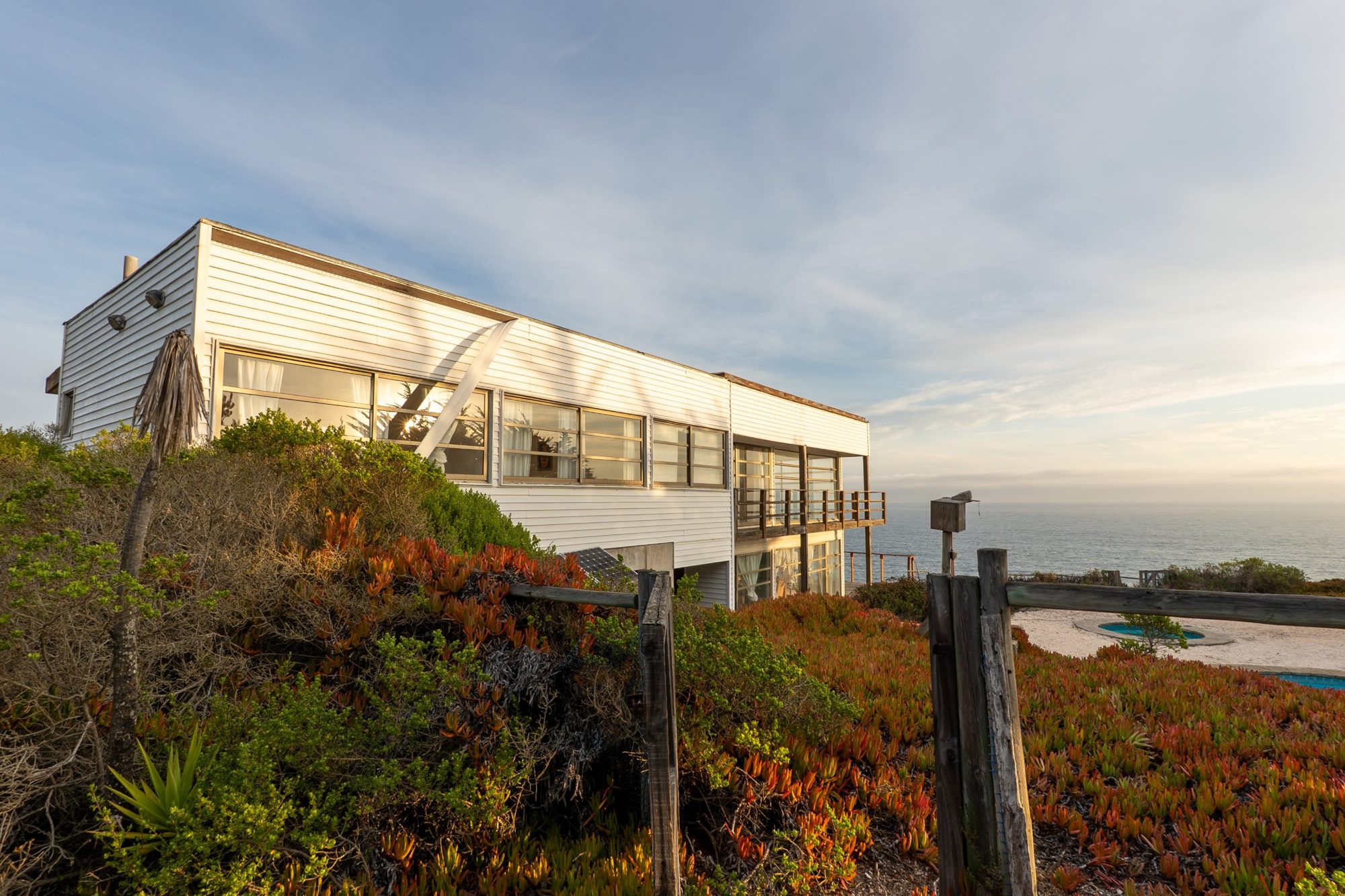 Casa blanca de madera sobre un acantilado frente al mar al atardecer